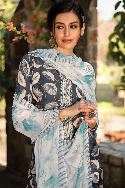 A woman wearing a traditional three-piece suit set in light blue, white, and navy with a leaf pattern, standing outdoors in front of a blurred stone wall and greenery. | Wholesale Embroidered Kurta Set for Women | Sri Fashion