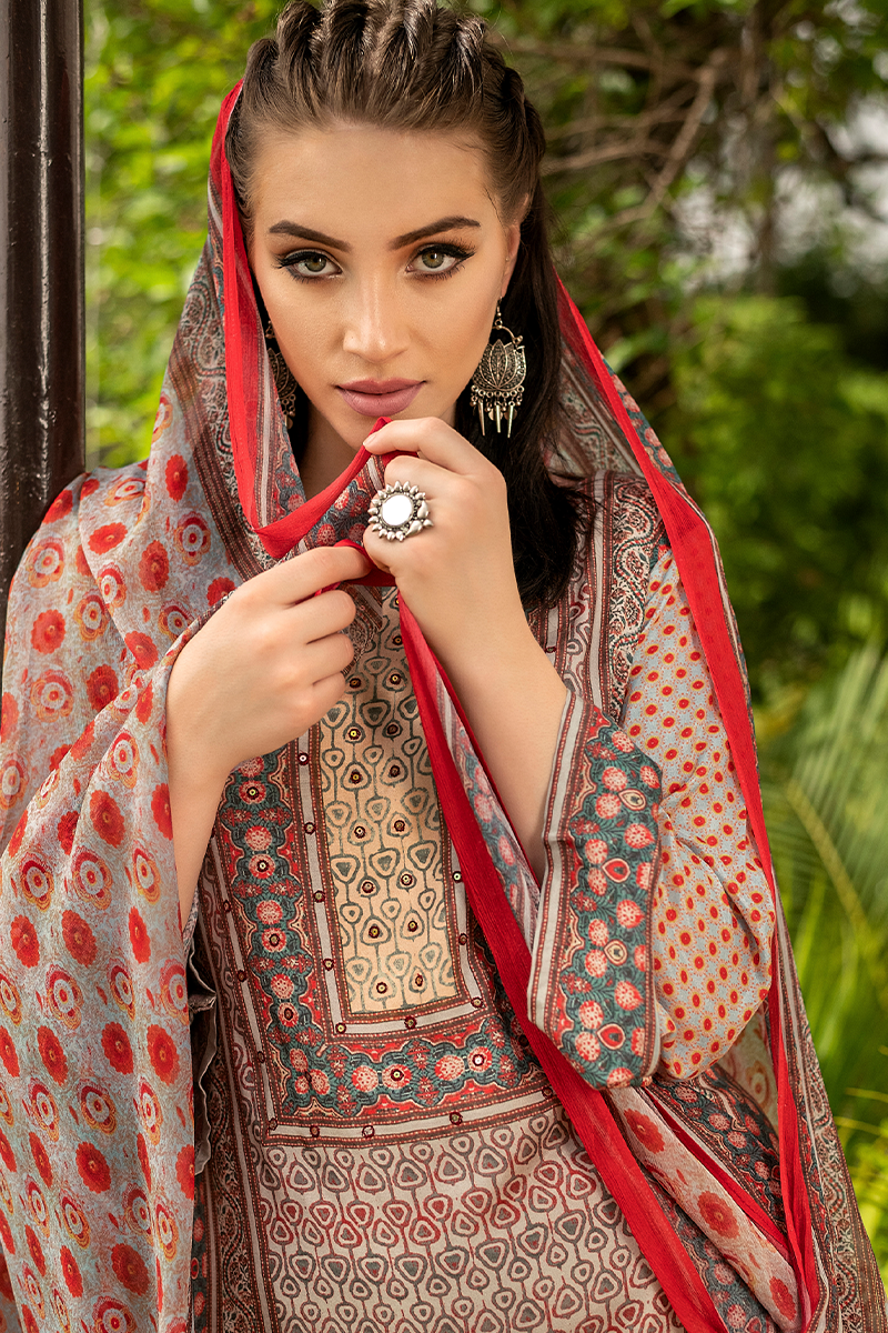 A woman wearing a traditional South Asian suit set outfit in beige, red, and teal with a matching patterned dupatta, set against a blurred green outdoor background. | Wholesale Beige Ethnic Muslin Suit Set | Sri Fashion
