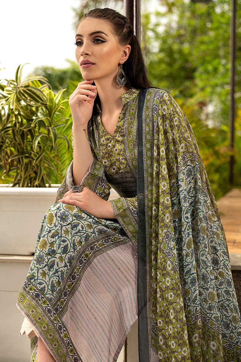 A woman wearing a traditional South Asian outfit with an olive green and gray paisley printed dupatta and matching blouse, paired with a striped skirt, posed outdoors against a green garden background. | Wholesale Olive Green Ethnic Muslin Suit Set | Sri Fashion