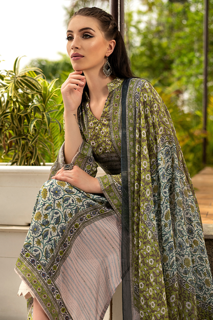 A woman wearing a traditional South Asian outfit with an olive green and gray paisley printed dupatta and matching blouse, paired with a striped skirt, posed outdoors against a green garden background. | Wholesale Olive Green Ethnic Muslin Suit Set | Sri Fashion